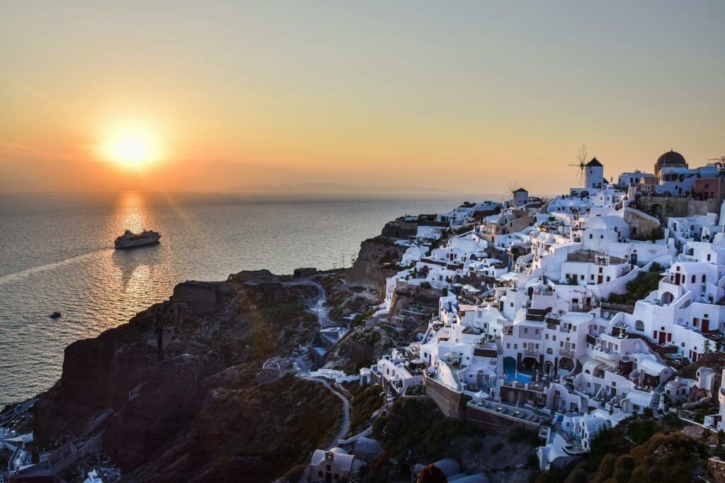 Beautiful sunset view of Santorini's whitewashed buildings and a cruise ship in the Aegean Sea.